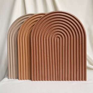 Pode incluir: Três bandejas decorativas em forma de arco feitas de concreto. As bandejas são em tons de bege, marrom e terracota. As bandejas são revestidas de ranhuras e têm uma superfície texturizada.