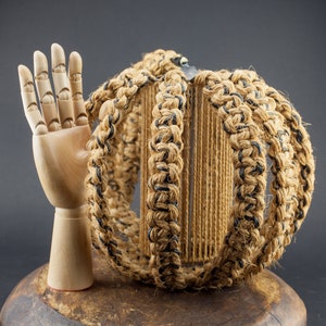 May include: A wooden hand model with a raised palm, standing next to a round, woven lampshade made of natural jute rope with black accents.