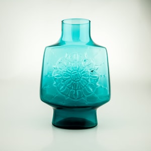 Op de afbeelding: Een tealblauwe glazen vaas met een geometrisch ontwerp. De vaas heeft een brede basis en een smalle hals.