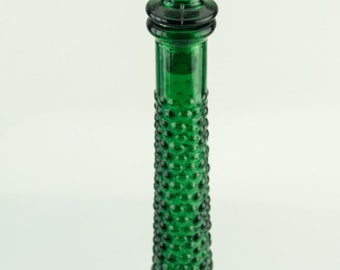 May include: A tall, green glass bottle with a textured, bubble-like surface. The bottle has a narrow neck and a rounded base.