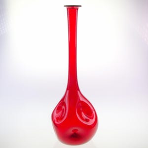 Può includere: Un vaso alto in vetro rosso con una base bulbosa e irregolare. Il vaso ha una finitura liscia e lucida.