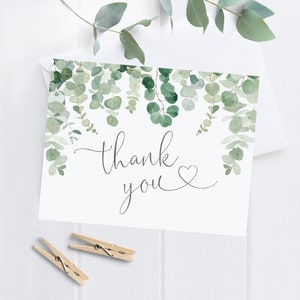 May include: A white thank you card with a green watercolor eucalyptus garland design and the text "thank you" with a small heart.