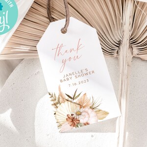 May include: A white thank you tag with a pink script font that says "Thank you". Below the text is the name "Janelle's Baby Shower" and the date "7.16.2023". The tag is decorated with a watercolor illustration of dried flowers and leaves in shades of brown, beige, and pink.