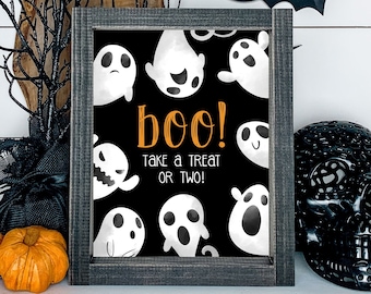 May include: A rectangular sign in a dark grey wooden frame featuring a black background with white cartoon ghosts and the orange text "boo!" followed by the white text "TAKE A TREAT OR TWO!" displayed in a clear, sans-serif font.