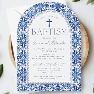 May include: Baptism invitation card with a blue and white floral design. The invitation has an arched shape and includes the text "Baptism of our son" and event details. The card is on a wooden tray with greenery.