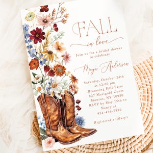 May include: A rectangular bridal shower invitation featuring a watercolor illustration of brown leather cowboy boots filled with autumn-toned wildflowers. The text reads: FALL in love, Join us for a bridal shower to celebrate Maya Andersen, Saturday, October 24th at 12:00 pm, Blooming Hill Farm, 827 Marigold Court, Monroe, NY 10950, RSVP by May 15th to Nancy at 954-456-7890, Registered at Macy's.