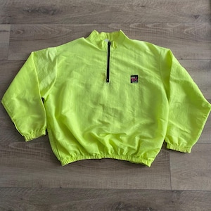 Op de afbeelding: Een felgele windjack met een zwarte rits en een kleine logopatch. De jas heeft een hoge kraag en elastische manchetten en zoom. De windjack is gemaakt van een lichtgewicht materiaal, mogelijk nylon.