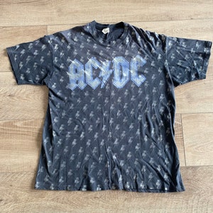 Puede incluir: Camiseta negra con un logotipo "AC/DC" azul y blanco y un patrón de rayos.