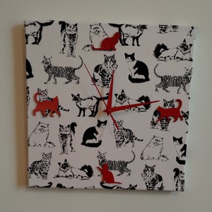 May include: A white canvas clock with black and white cat silhouettes and red cat-shaped clock hands.