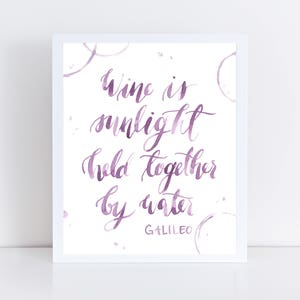 May include: White framed art print with the quote "Wine is sunlight held together by water" in purple calligraphy. The print includes purple watercolor accents and the name "Galileo" at the bottom.
