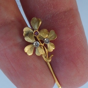 Op de afbeelding: Een gouden broche met een cluster van drie klaverbladvormige bladeren met rode en witte edelstenen.