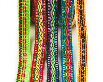 May include: Assortment of colorful woven ribbon trim with geometric patterns. The ribbons are in shades of green, red, blue, black, and white.