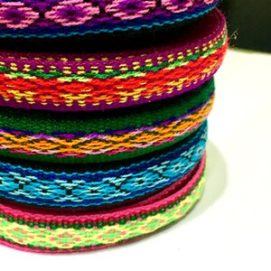 May include: A stack of colorful woven trim with intricate patterns in shades of pink, green, blue, yellow, orange, and red.