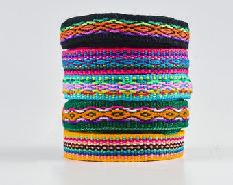May include: A stack of colorful woven bands with geometric patterns. The bands are made of different colors, including black, green, orange, pink, blue, and yellow.