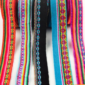 Op de afbeelding: Vijf kleurrijke geweven lintversieringen met geometrische patronen. De linten zijn rood, blauw, zwart, turquoise en regenboogkleurig.