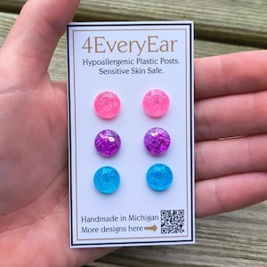 May include: A card with six pairs of colorful glitter stud earrings. The earrings are pink, purple, and blue. The card reads "4EveryEar" and "Hypoallergenic Plastic Posts. Sensitive Skin Safe." It also says "Handmade in Michigan."
