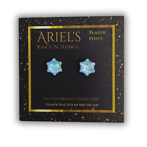May include: A pair of snowflake stud earrings with light blue crystals on plastic posts. The earrings are packaged on a black card with gold lettering that reads "Ariel's Rings 'n Things" and "Hypoallergenic Collection Handcrafted in Michigan".