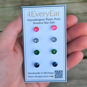 May include: A card displaying six pairs of stud earrings in various colors: pink, silver, green, and teal. The card reads "4EveryEar" and "Hypoallergenic Plastic Posts. Sensitive Skin Safe." It also says "Handmade in Michigan."