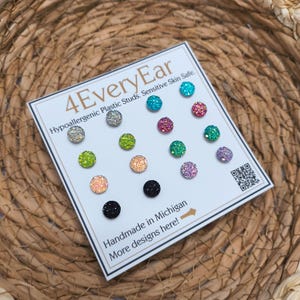 May include: A set of 12 glitter-covered stud earrings in various colors, including silver, teal, pink, green, and purple. The earrings are displayed on a white card with the text "4EveryEar" and "Handmade in Michigan".