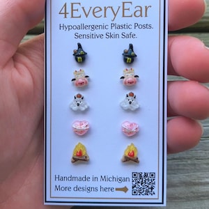 May include: A card displaying several pairs of hypoallergenic plastic post earrings. The earrings feature various designs, including a witch's hat, a cow, a ghost, a heart, and a campfire. The card reads "4EveryEar" and "Handmade in Michigan."