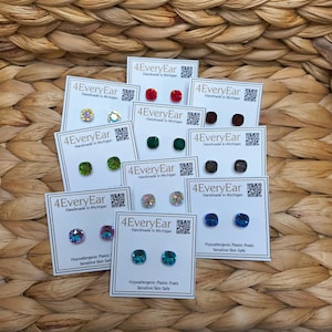 Pode incluir: Uma coleção de brincos de pressão em cartões brancos, cada um exibindo o logotipo "4EveryEar Handmade in Michigan". Os brincos apresentam várias cores, incluindo opções vermelhas, verdes, azuis e iridescentes. Os cartões também indicam "Hypoallergenic Plastic Posts Sensitive Skin Safe."