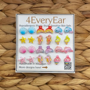Può includere: Una scheda espositiva con l'etichetta 4EveryEar che presenta venti piccoli orecchini a perno in plastica colorata con varie forme marine, tra cui conchiglie, stelle marine, cavallucci marini, delfini e lumache di mare, con una finitura lucida.