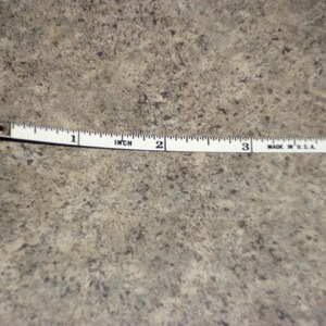 Pu&ograve; includere: Un metro a nastro bianco con segni neri, che mostra pollici. Il nastro misura fino a 10 cm. Il nastro &egrave; su una superficie strutturata dai toni neutri.