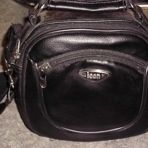 May include: Black leather shoulder bag with a textured finish. The bag has a rounded front with a zippered pocket and a silver-toned Icon logo. It features a top handle and a detachable shoulder strap.