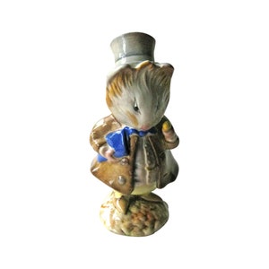 May include: A ceramic figurine of a brown and white rabbit wearing a brown coat, a blue bow tie, and a gray top hat. The rabbit is holding a yellow object in its right paw and a blue book in its left paw. The rabbit is standing on a brown and yellow base.
