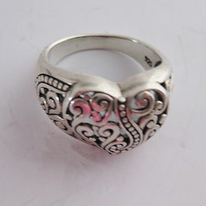 May include: A silver ring with a heart-shaped design featuring intricate scrollwork and a textured finish.