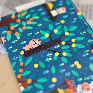 May include: A teal-colored zippered pouch with a whimsical tree and animal print. The design features a sleeping bear on a tree branch, orange fruits, and green leaves. The pouch has a white zipper and a gold-colored pull.
