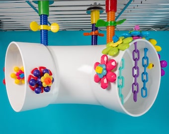May include: A white plastic pipe with colorful plastic flowers and chains attached. The pipe is hanging from a metal rack.