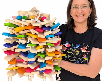 May include: A large bird toy constructed from numerous rectangular wooden blocks in vibrant shades of red, orange, yellow, green, blue, and purple, interspersed with natural wood pieces and held together by thick white cotton rope with knotted ends.