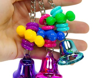 May include: A colorful bird toy with a chain and three bells. The toy features a series of plastic beads in various colors, including purple, yellow, blue, pink, and green. The bells are silver and have a shiny finish.