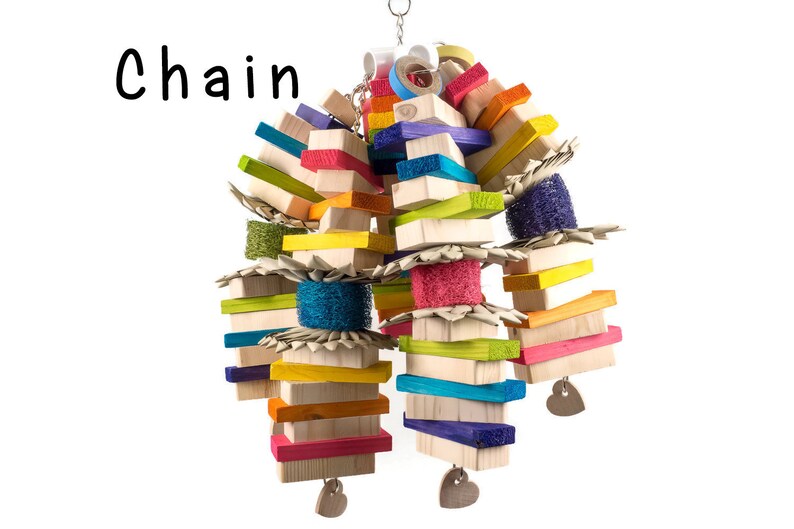 May include: A colorful wooden bird toy with a chain, featuring various shapes and textures, including wood blocks, colorful sponges, and woven straw. The toy is designed for birds to play with and features a heart-shaped charm.