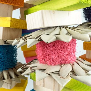 May include: A colorful wooden bird toy with different textures and colors. The toy features a variety of natural materials, including wood, sisal rope, and woven palm leaves.