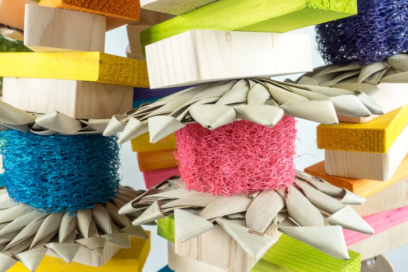 May include: A colorful wooden bird toy with different textures and colors. The toy features a variety of natural materials, including wood, sisal rope, and woven palm leaves.