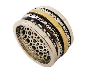 May include: A silver and gold-tone ring with a unique design. The ring features a gold band in the center, surrounded by silver bands with etched patterns and text. The lower portion of the ring has a decorative openwork design.