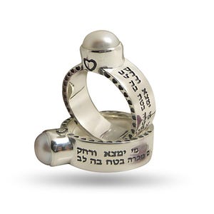 Op de afbeelding: Twee zilveren ringen met elk een parel. De ringen zijn gegraveerd met Hebreeuwse tekst. De bovenste ring heeft een hartvorm aan de zijkant. De tekst op de bovenste ring is "Mi Shebeirach" en de tekst op de onderste ring is "Mi Shebeirach Et Sarah Im Tzeira."