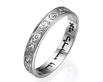 May include: A silver band ring with an intricate floral design engraved around the band. The inside of the band is inscribed with Hebrew text.