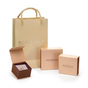 May include: A set of three boxes for jewelry and Judaica. The boxes are all beige with gold lettering. The largest box is a shopping bag with a gold rope handle. The smaller boxes are square and rectangular. The text on the boxes reads "Balitnester: Jewelry & Judaica".