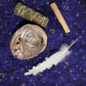 May include: An arrangement of spiritual items on a dark blue fabric with a starry pattern. The items include a sage bundle, a piece of palo santo wood, an abalone shell, and a white feather.