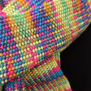 May include: A woven textile fabric featuring a vibrant, multi-colored pattern of intersecting threads in shades of bright pink, lime green, orange, turquoise, and purple. The material displays a dense, textured weave with a repeating geometric design.