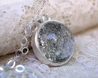 May include: A silver chain necklace with a round pendant featuring a clear glass dome filled with silver glitter.