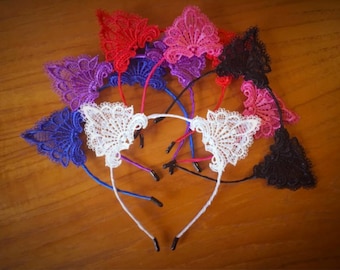 May include: Set of eight cat ear headbands with lace trim in various colors, including black, white, blue, purple, and pink. The headbands are made of metal and have a simple design.