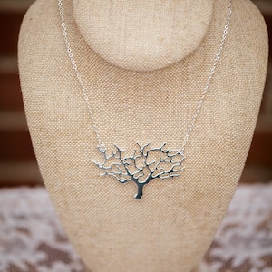 May include: A silver necklace with a tree-shaped pendant. The pendant is made of a delicate, intricate design and hangs from a silver chain.
