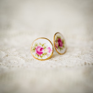 May include: A pair of white porcelain earrings with gold trim and a pink floral design.