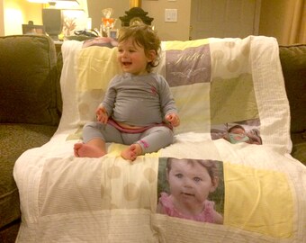 May include: A white and yellow patchwork quilt with a baby girl sitting on it. The quilt has a variety of patterns and colors, including stripes, polka dots, and flowers. The baby is wearing a gray shirt and has a happy expression on her face. The quilt has the name "Julia" written on it.