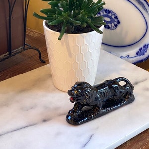 May include: A small green succulent plant in a white hexagonal patterned pot, a black panther figurine with red eyes, and two blue and white decorative plates. The items are arranged on a white marble surface against a yellow wall.