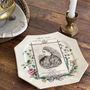 Könnte beinhalten: Ein antiker achteckiger Teller mit einem Porträt von Königin Victoria, mit Text, der das Jubiläumsjahr ab dem 20. Juni 1886 angibt. Der Teller ist mit floralen und Bandmotiven in Rosa, Grün und Blau verziert.